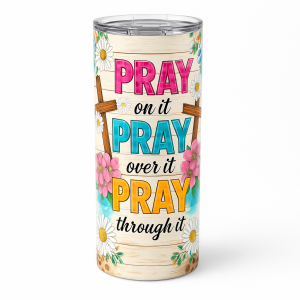 =Floral faith-themed tumbler with crosses and the phrase 'Pray on it, Pray over it, Pray through it' in bright pink, teal, and yellow letters on a light wood-look background.